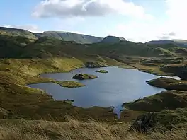 A small lake with two rocky islets surrounded by fells.