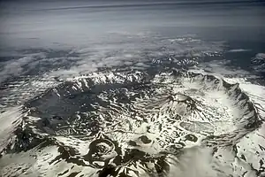 Aerial view of large, snowy crater, surrounded by mountains