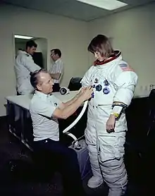 A technician adjusts an overly-large Apollo spacesuit