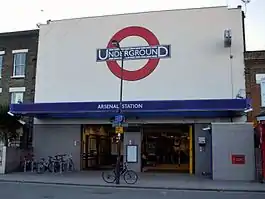 A light grey building with a sign stating "ARSENAL STATION" in white letters on a blue background and four bicycles laying idle in the foreground