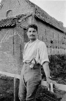 Photograph of a young man in shirt sleeves, leaning on a low wall.