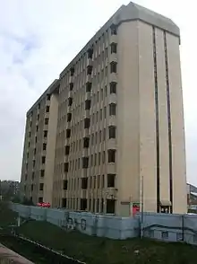 A nine-storey concrete office building sits behind a blue-painted retaining wall beside a railway cutting.