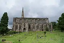 A stone church seen from the south with multiple large windows in the south aisle and clerestory, a two-storey south porch, and part of the spire beyond