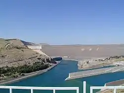 Aerial view of a large structure located between mountains and a large lake