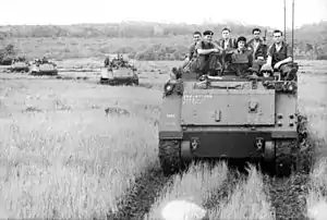 Black and white photo of three tracked military vehicles with men in military uniforms sitting on their roofs