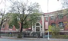 A two-story red brick building partially obscured by a tree on a cloudy day