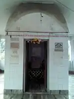 A tomb-like structure covered in while tiles with Bengali script at the entrance