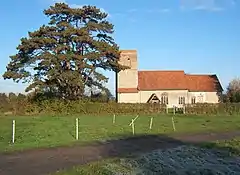 A stone church seen from the south with red tiled roofs and a plain tower on the left