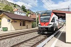 White-and-red train on double-track with single-story building at left