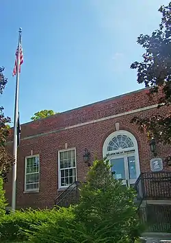 View of some of the front of the post office with a flagpole in front and some lens flare in the blue sky