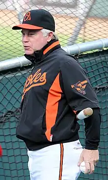 A man in a black baseball jersey, white pants, and black cap