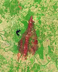 Satellite image of the burn scar, which appears as a large red and orange area within bright green vegetation using data that emphasizes the burn scar