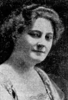 A white woman with a bouffant hairstyle, wearing a dress with a square neckline