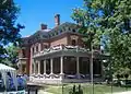 Red brick home with ornate white overhang supports, red-white-blue banners, and columned white porch