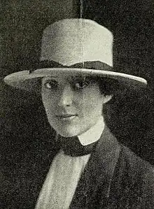 young white woman wearing a large brimmed hat and a tailored shirt and jacket.