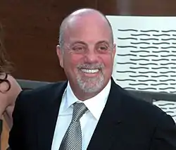 A bald man with a grey beard wearing a jacket and necktie, smiling broadly