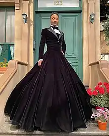 a man wearing a black velvet ball gown, the top half styled like a tuxedo, with a voluminous white-trimmed skirt