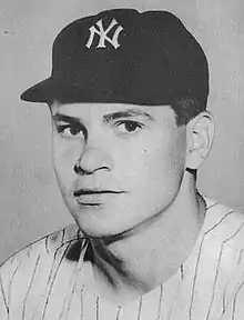 A man in a light baseball jersey and dark cap