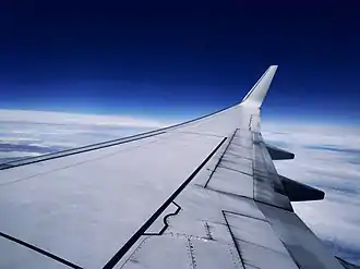 A generic Boeing 737-800 cruising at 32,000 feet. Below it is a pack of clouds. Above it is a vivid, ambient blue sky.