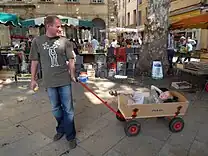 A man pulling a wooden cart with a child lying inside.