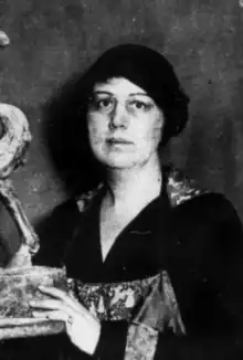 A white woman wearing a black beret and a black dress with a v-neckline