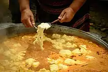 A large pot of orange-yellow borscht with thick doughy noodles