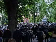 At least one hundred people, some with signs, gathered in a park