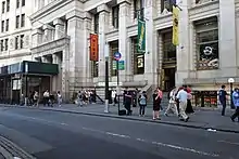 A Subway Restaurant and several stores in the building with a bus stop on the curb