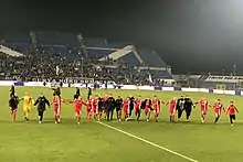 Smiling Monza players holding hands running towards the camera at night in a stadium