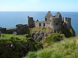 A ruin of a medieval castle on a high cliff over the sea. A round tower stands in front in the centre.