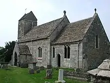 A stone church seen from the southeast, showing the chancel, beyond which is a nave with a higher roof and a porch and, beyond that, a tower with a saddleback roof