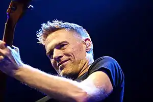  A close up color photo of a man playing the guitar, wearing a black T-shirt .