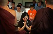 Asian person holding hands in prayer, facing two monks in brown robes.