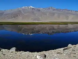 Image of Bukunkul lake taken from the shoreline, with the Pamir mountains reflecting on the surface of the lake.