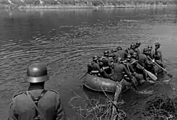 A black and white photograph of a group of German soldiers paddling a rubber boat across a river