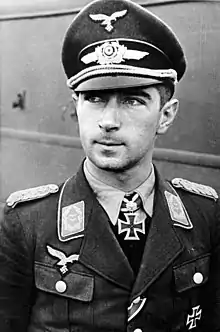 The head and shoulders of a young man. He wears a uniform and peaked cap, with an Iron Cross displayed at the front of his shirt collar.