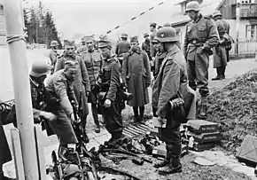 A black and white photograph of German soldiers watching other soldiers laying down their rifles in a pile