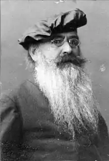 An elderly, bearded white man wearing glasses and a beret