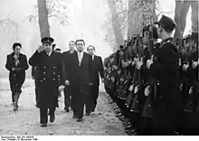 politicians walk in snow, past an honour guard with rifles