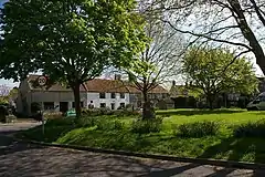 Grassy area with trees in the foregound and a terrace of stone houses, one white fronted, in the background