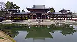 Wide wooden building on an island consisting of a central structure connected on either side to open corridors with towers at the end.