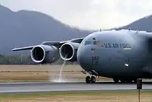 Vehicles and personnel unloading supplies from three gray C-17s parked together for victims of Hurricane Katrina.