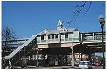 A green station house in a Queen Anne style, with a staircase on the left side leading up to it.