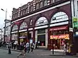 A red-bricked building with a blue sign reading "CAMDEN TOWN STATION" in white letters and a red sign reading "FIRST CHOICE RESTAURANT" in white letters