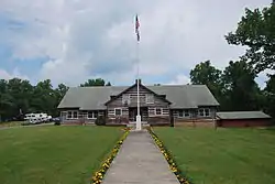 Photograph of the two-story log-cabin Great Chestnut Lodge at Camp Washington-Carver Complex, with a sidewalk, marigolds, and flagpole in the foreground