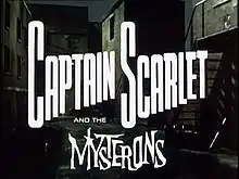 In bold, white letters, the words "Captain Scarlet" are superimposed on the backdrop of a derelict, night-time alleyway. Added at the bottom of the picture are more words, "and the Mysterons", the last of which is in white, spiky lettering. The full title is thus revealed to be "Captain Scarlet and the Mysterons".