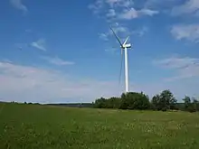 Wind turbine in open field, with turbines on the ridgeline in the background as well.