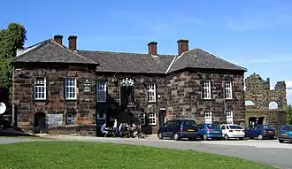 A stone building with protruding lateral wings, and a coat of arms in the centre