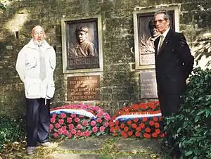 Two men in formal dress standing by a memorial.