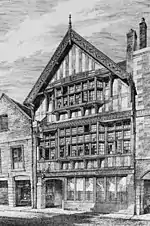 A black-and-white drawing of a three-storey timber-framed building seen from an angle. The lowest storey has a door on the left with a series of windows to the right; glazing extends across the middle storey, with a wide oriel window in the centre; the top gabled storey also contains an oriel window and at the top is an elaborately carved bargeboard.